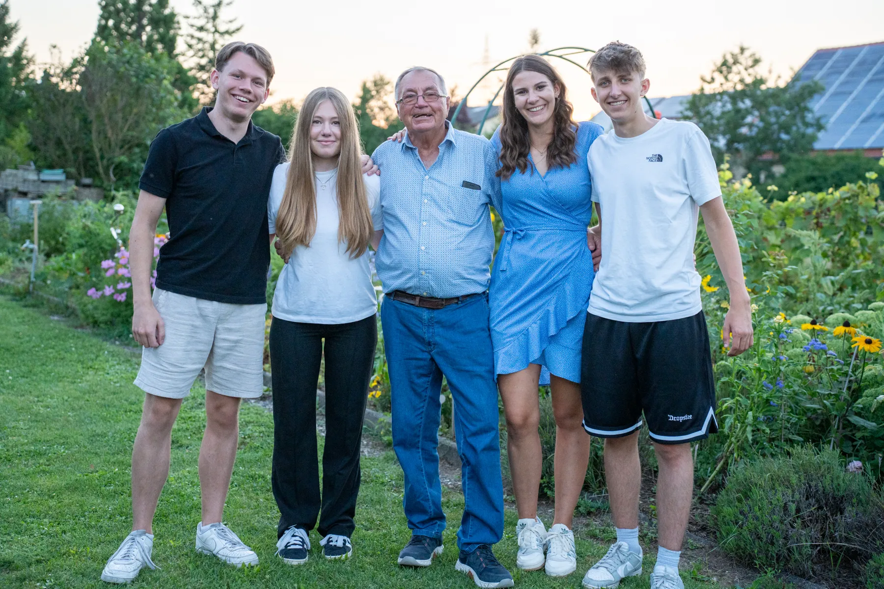 Fünf Personen, darunter ein älterer Mann, posieren gemeinsam draußen, alle lächeln.