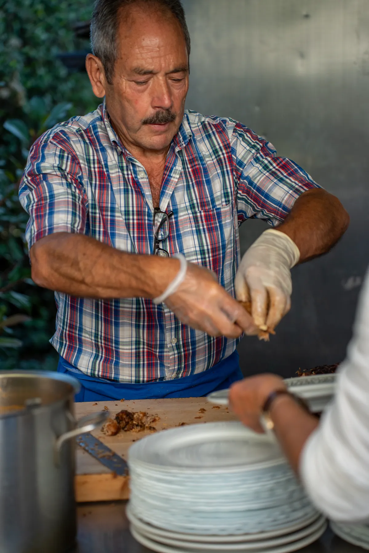 Ein Mann in kariertem Hemd bereitet Fleisch mit Handschuhen an einem Tisch zu.