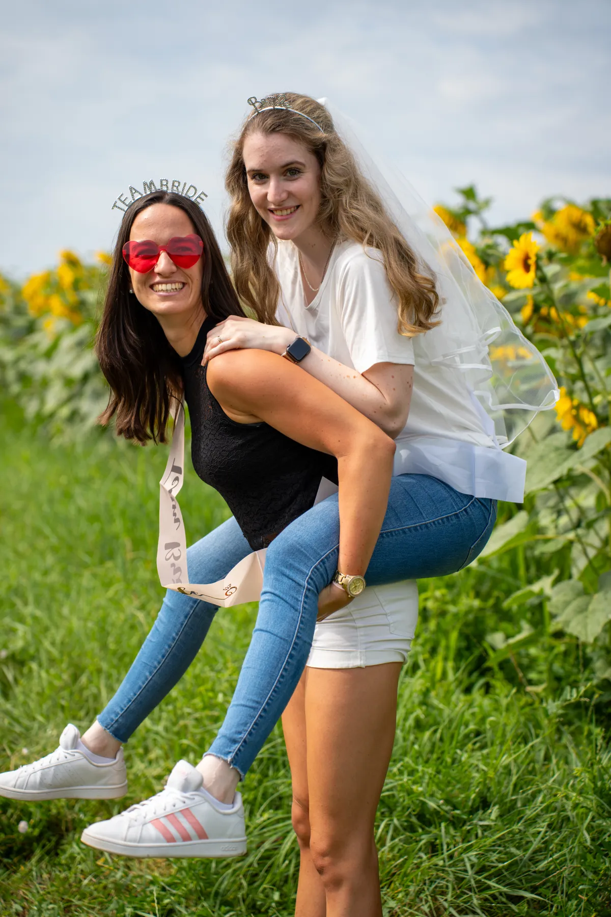 Zwei junge Frauen lachen, eine trägt die andere auf dem Rücken, beide sind leger gekleidet.