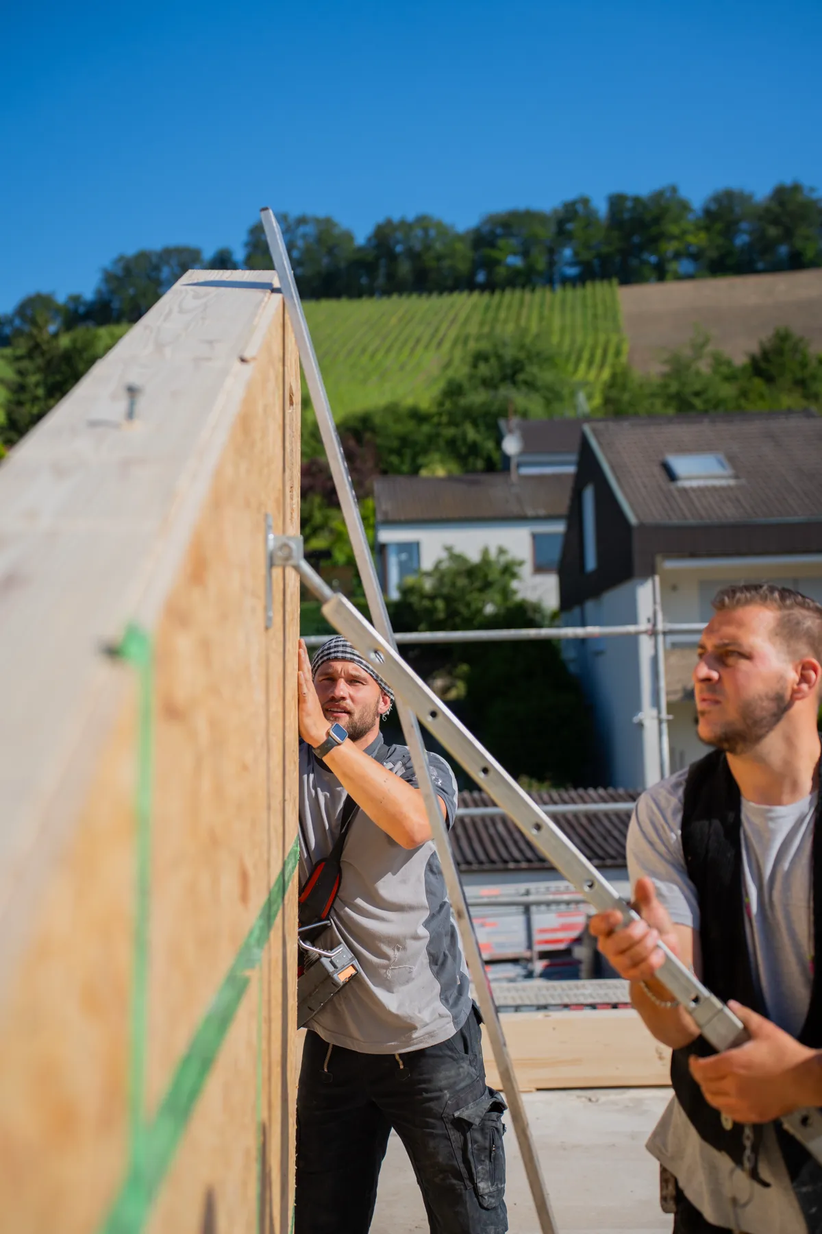 Zwei Männer richten Holzrahmenwand auf Baustelle aus.