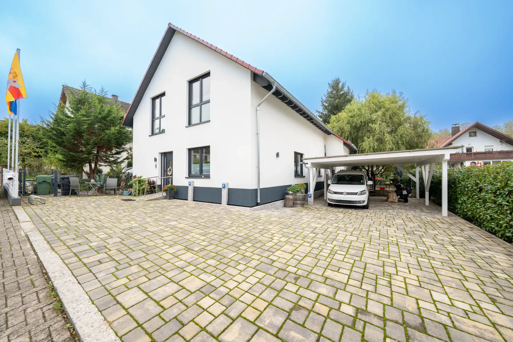 Weißes Einfamilienhaus mit rotem Dach und großem gepflastertem Hof.
