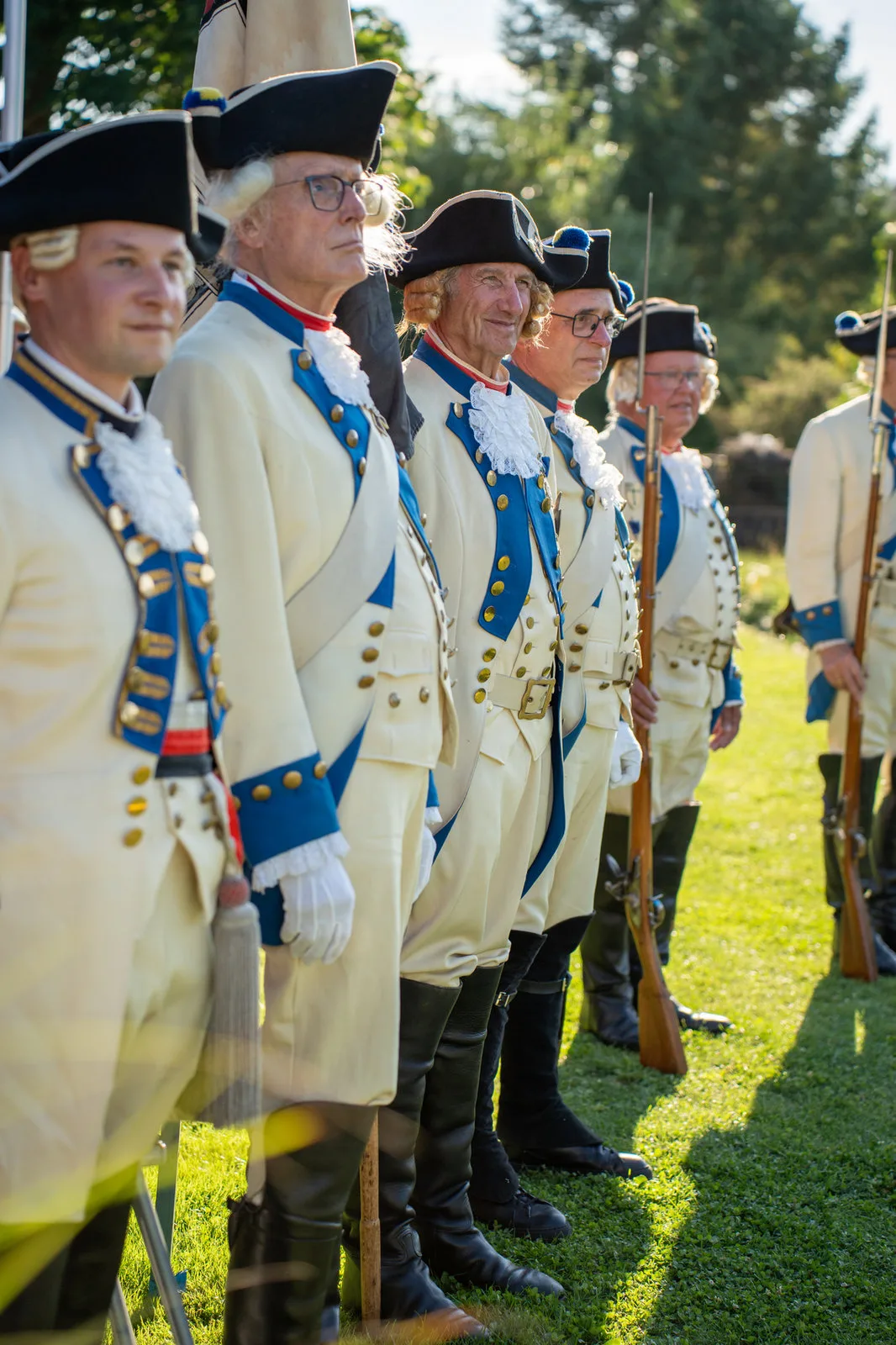 Mitglieder einer historischen Garde in weiß-blauen Uniformen mit Dreispitz stehen in einer Reihe.