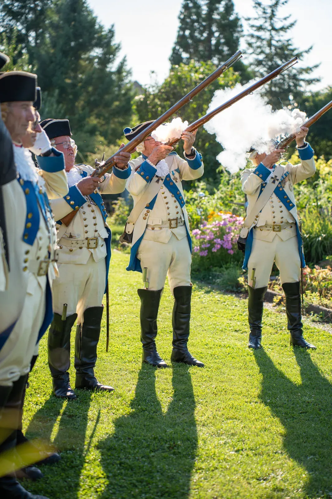 Gardisten in historischen Uniformen feuern einen Salut, Pulverrauch steigt über den Musketen auf.