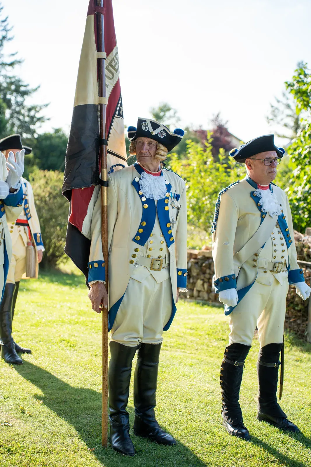 Der Fahnenträger der Garde hält die Standarte, neben ihm steht ein Gardist mit Brille in Uniform.