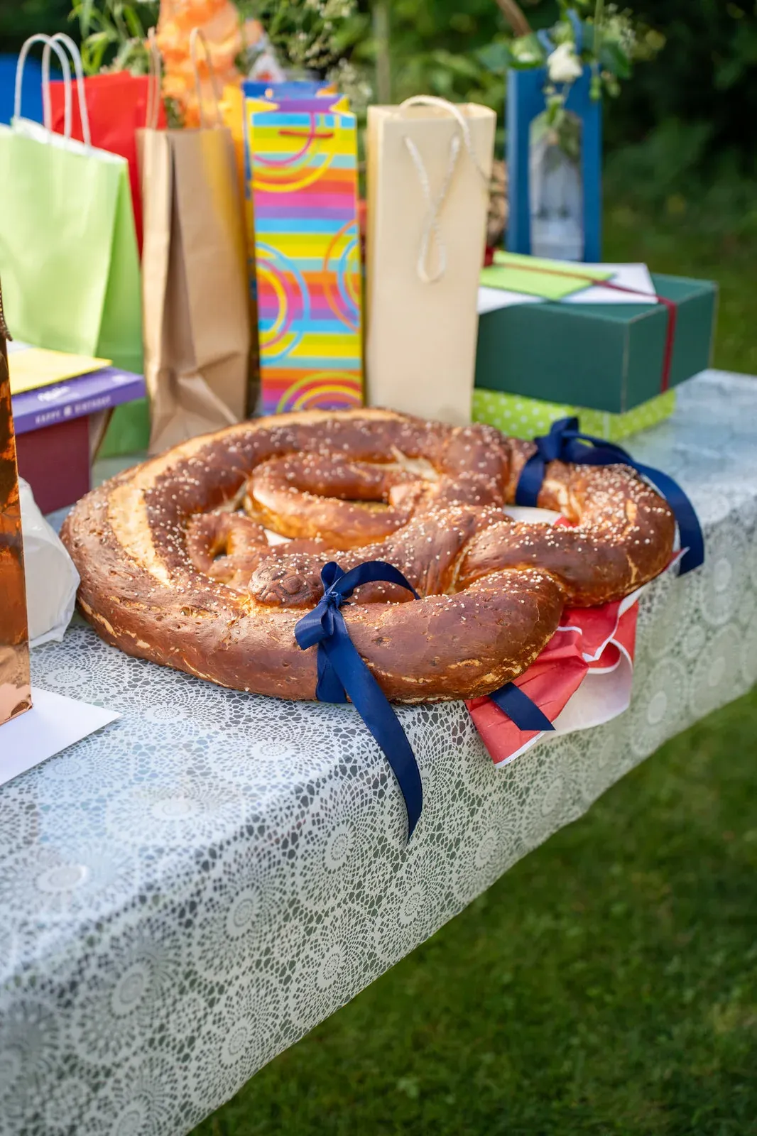 Eine große Festbrezel mit blauen Schleifen liegt auf dem Geschenktisch zwischen bunten Tüten.