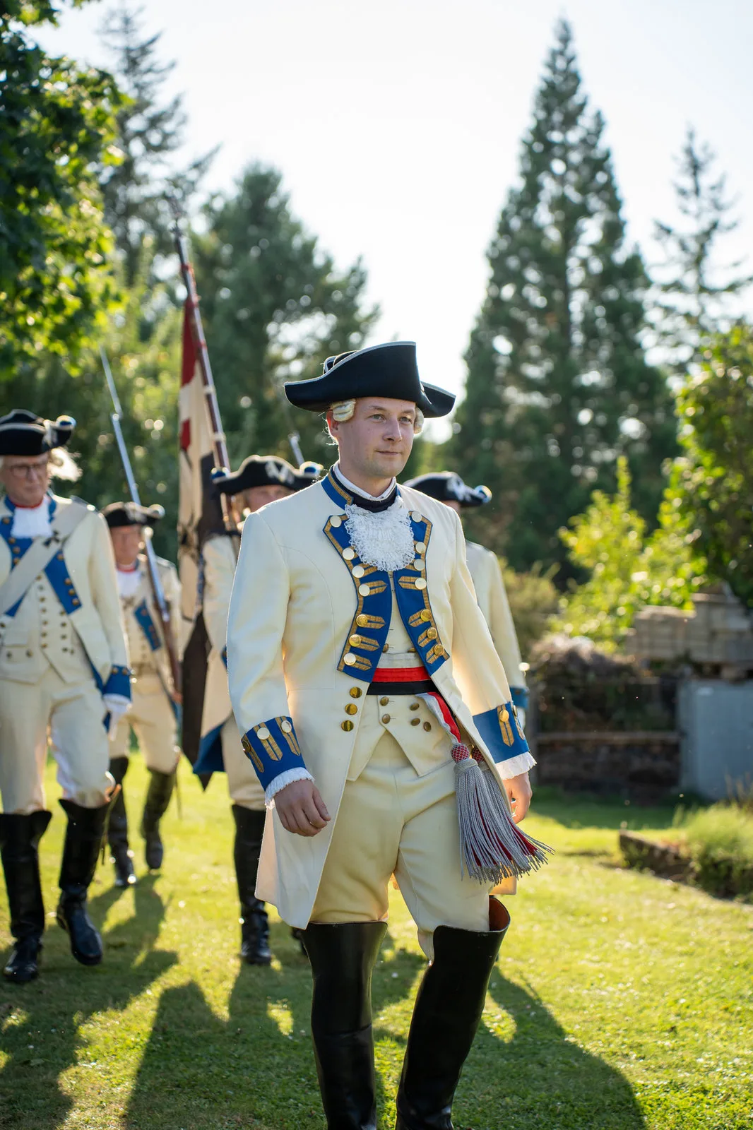 Ein junger Gardist in heller Uniform mit Dreispitz führt den Zug an, hinter ihm die Fahne.