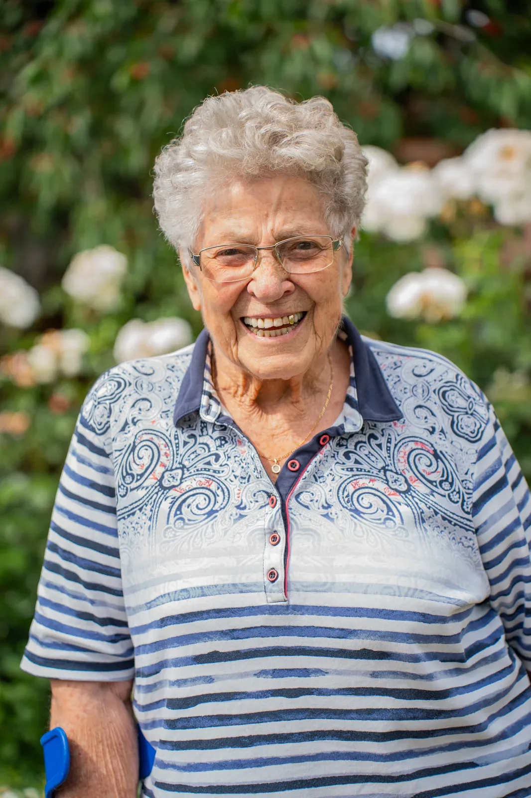 Portrait einer herzlich lachenden Seniorin mit Brille vor weiß blühenden Rosen.