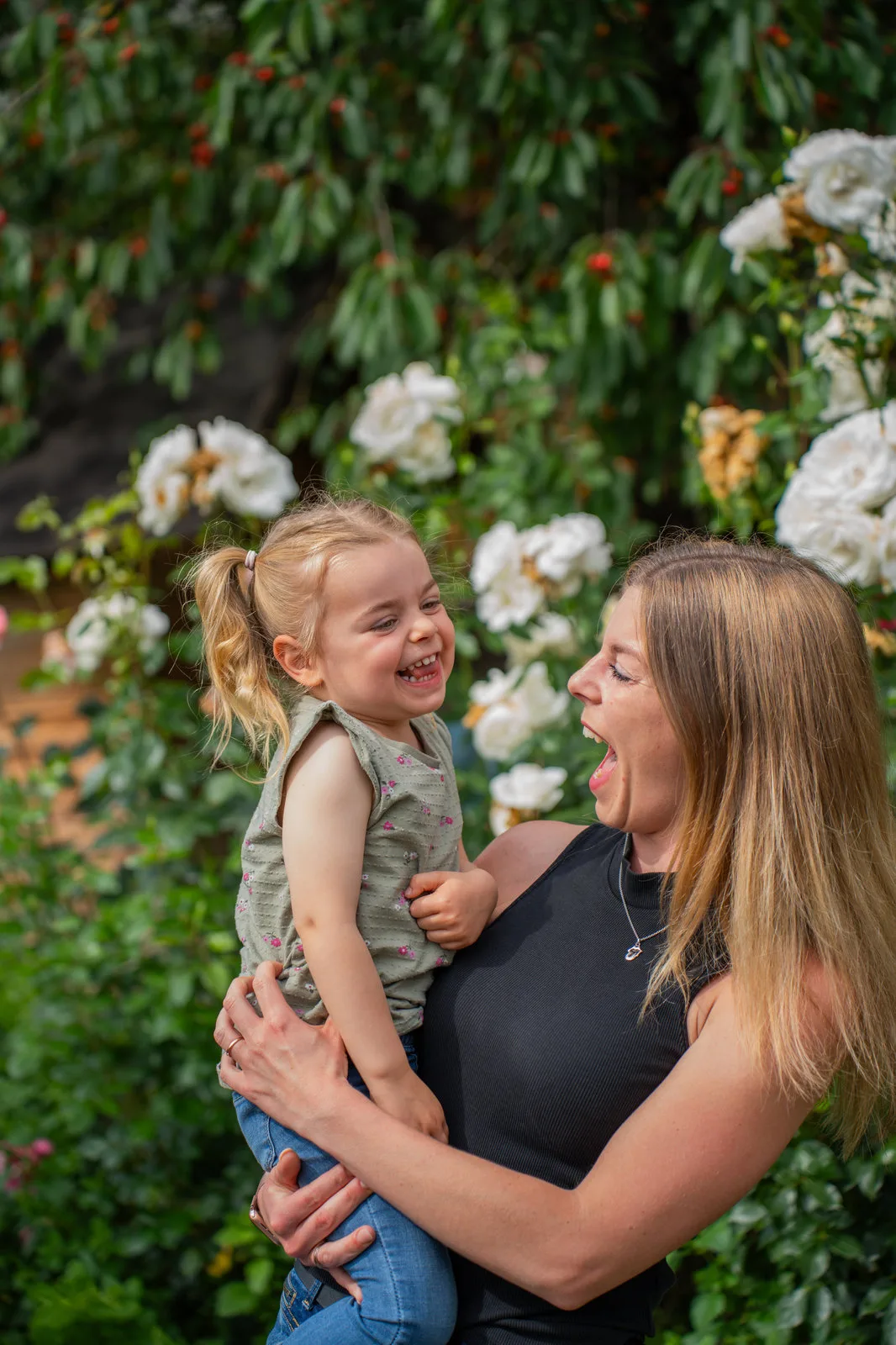 Mutter und Tochter lachen sich vor blühenden Rosen herzlich an.