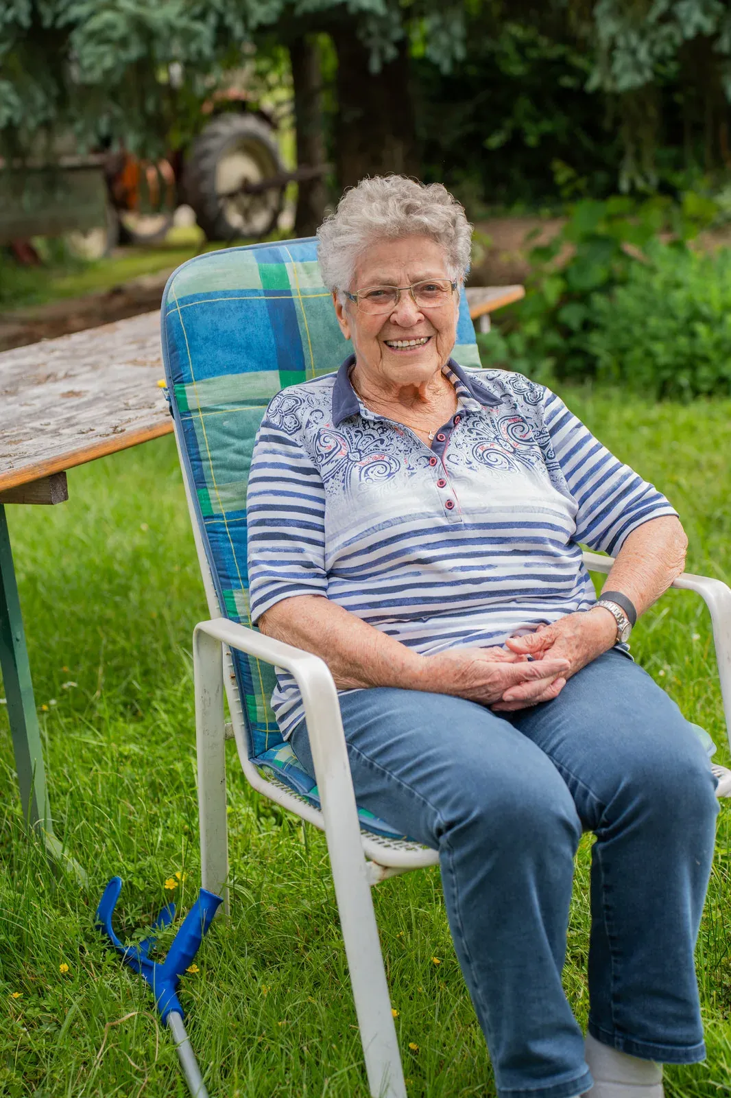 Eine Seniorin sitzt entspannt lächelnd im Gartenstuhl auf der Wiese.