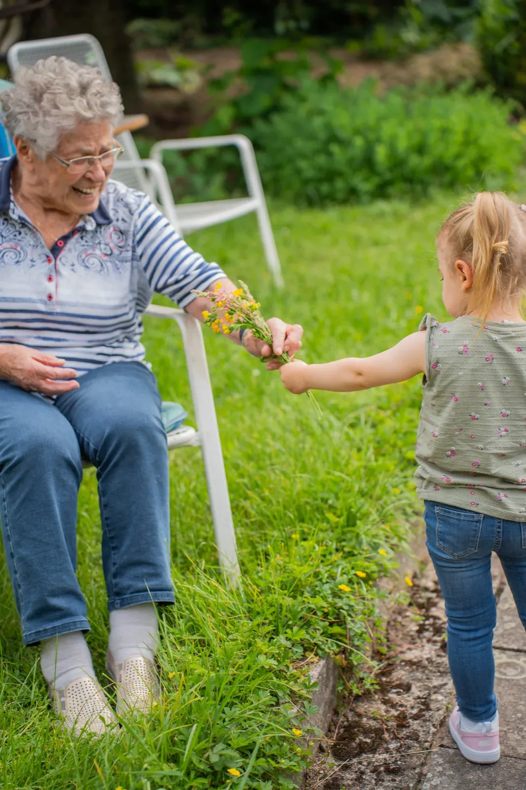 Das Enkelkind überreicht der Großmutter einen kleinen Strauß Wiesenblumen im Garten.