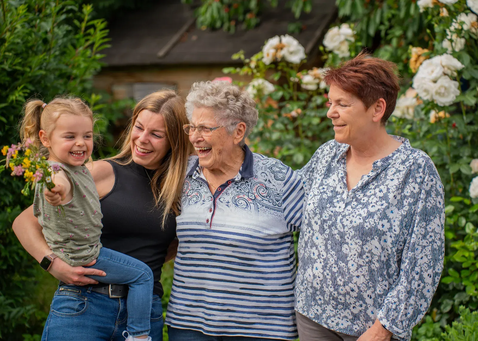 Vier Generationen einer Familie stehen lachend beieinander im Rosengarten.