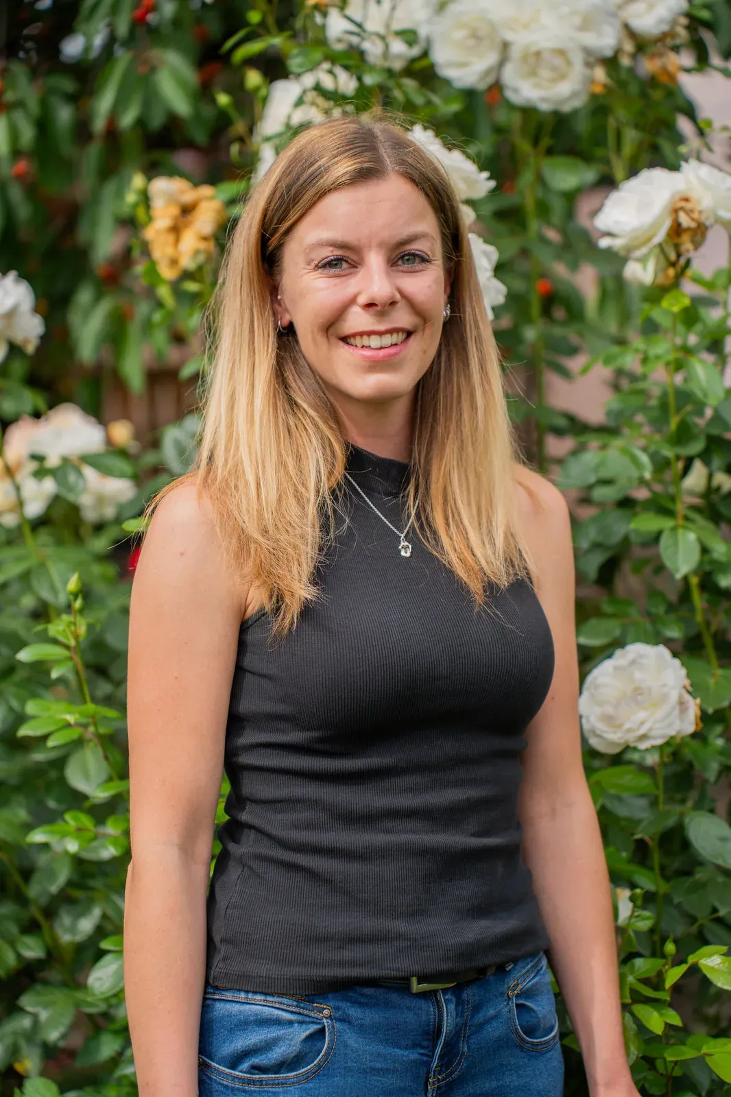 Portrait einer jungen Frau im schwarzen Top vor weiß blühenden Rosen.
