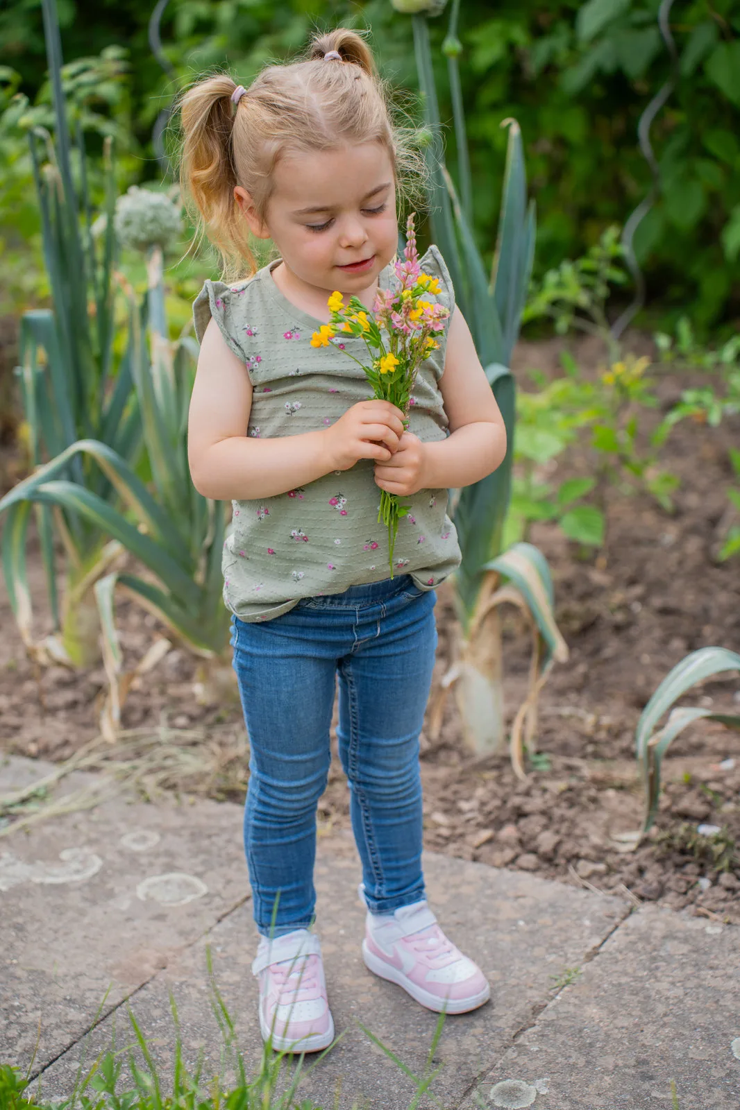 Ein Mädchen betrachtet versunken seinen kleinen Wiesenblumenstrauß im Gemüsegarten.