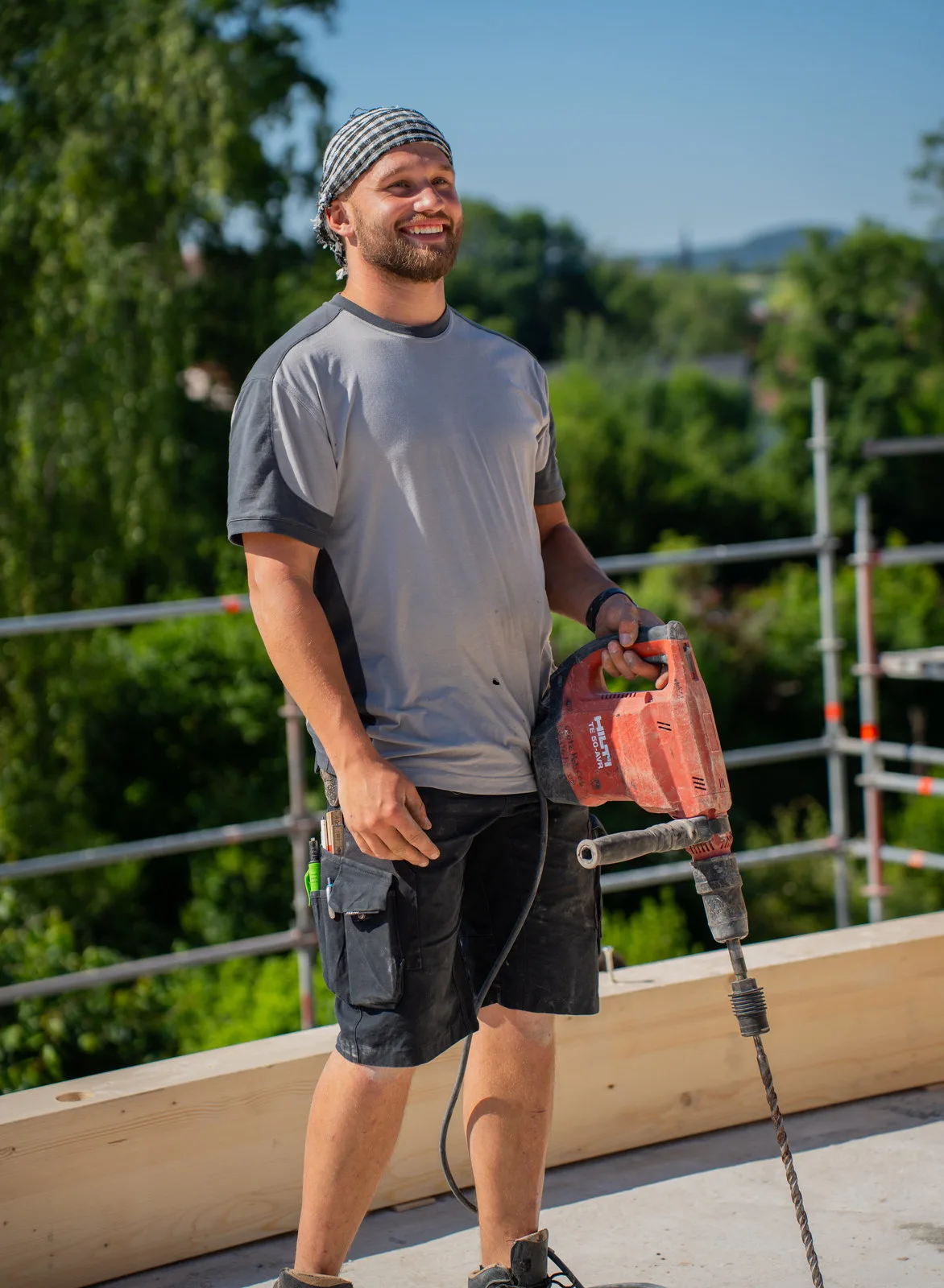 Ein Zimmermann mit Kopftuch steht lächelnd mit Bohrhammer auf dem Rohbau.