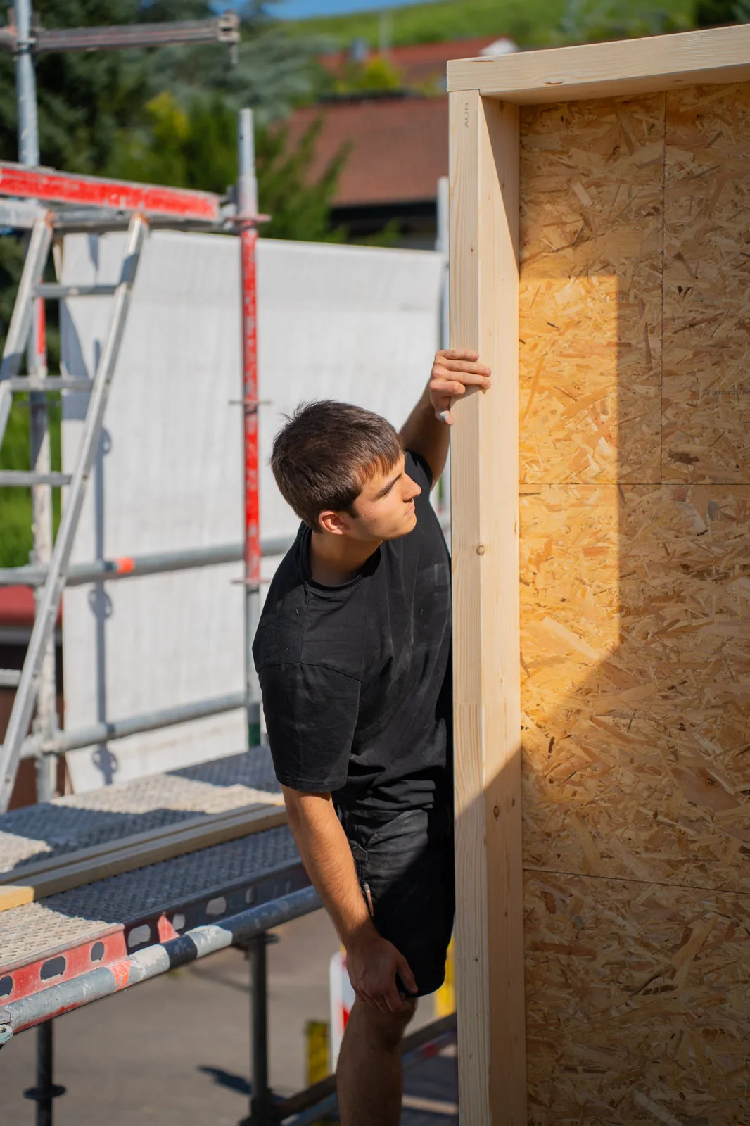 Ein junger Zimmermann richtet ein Holzwandelement auf dem Gerüst aus.