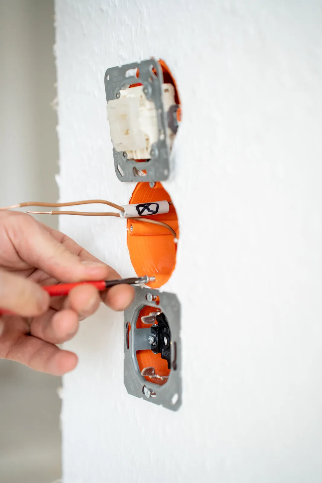 Ein Elektriker verdrahtet orangefarbene Unterputzdosen und hält einen Schraubendreher bereit.