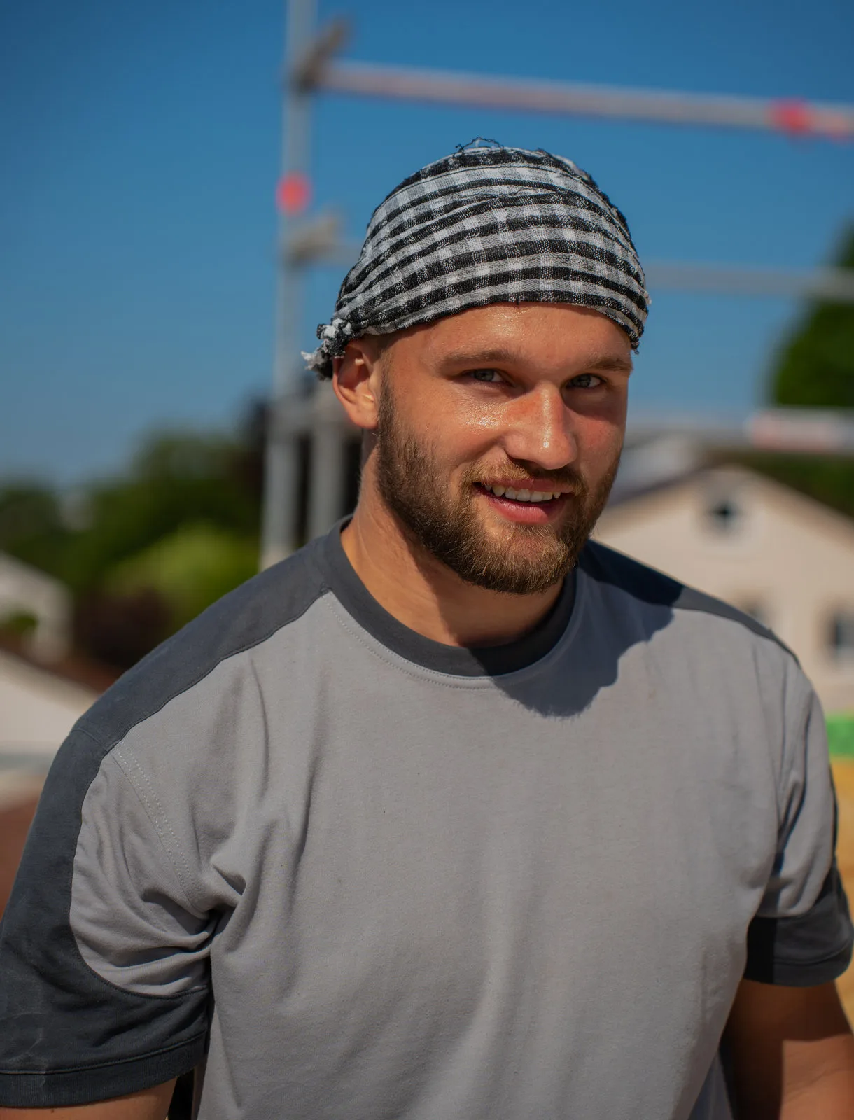 Portrait eines jungen Zimmermanns mit kariertem Kopftuch auf der sommerlichen Baustelle.