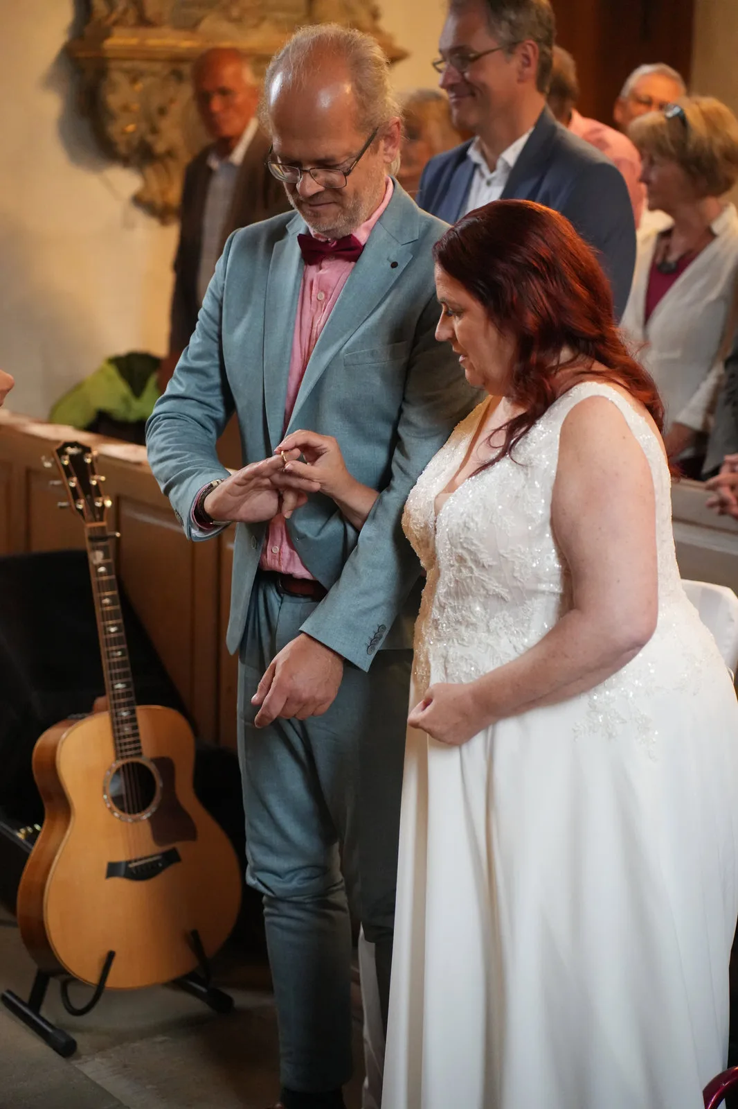 Ringtausch in der Kirche: Der Bräutigam in graublauem Anzug steckt der Braut den Ring an.