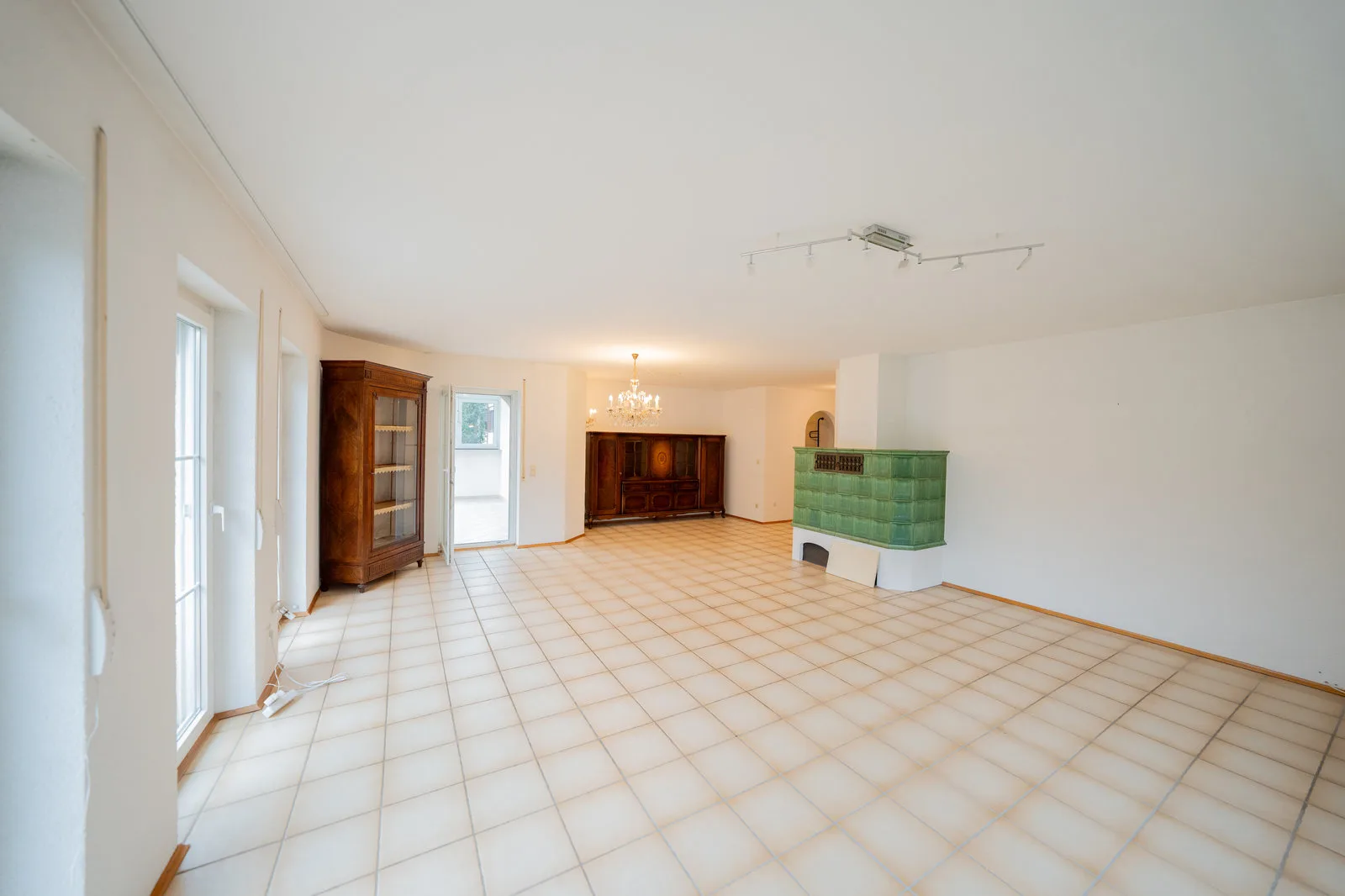 Großzügiges Wohnzimmer mit grünem Kachelofen, Kronleuchter und antiken Schränken.