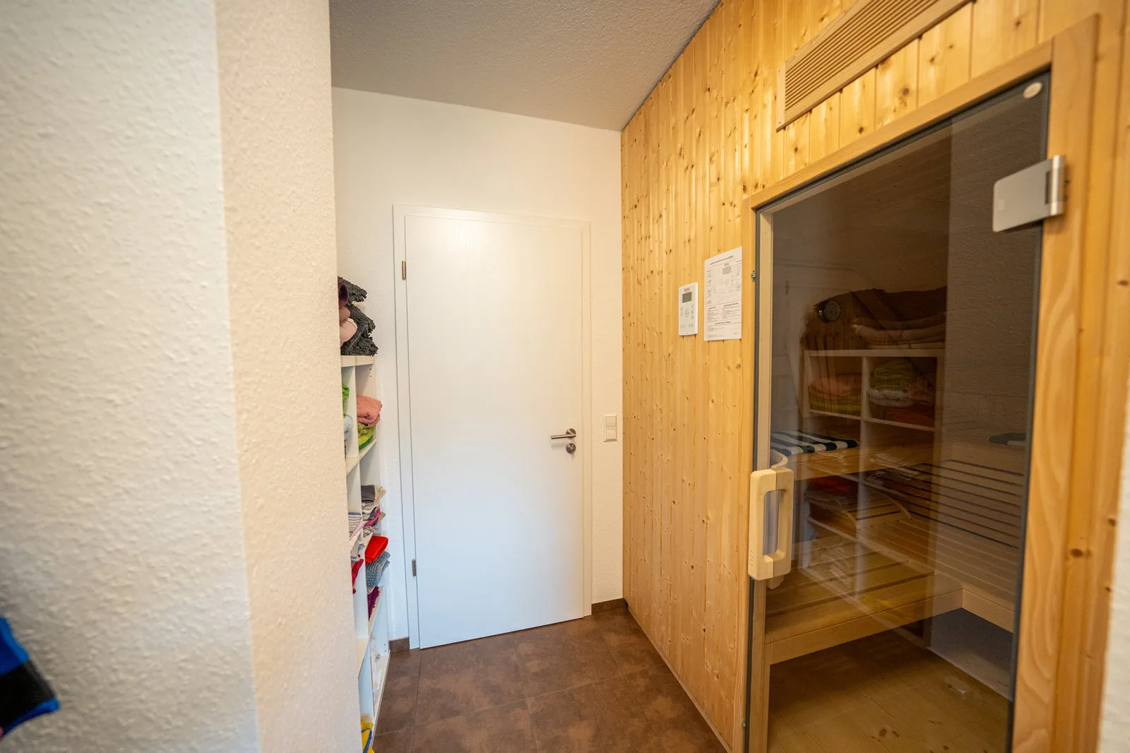 Blick in den Wellnessbereich: Sauna mit Glastür und Handtuchregal im Flur.