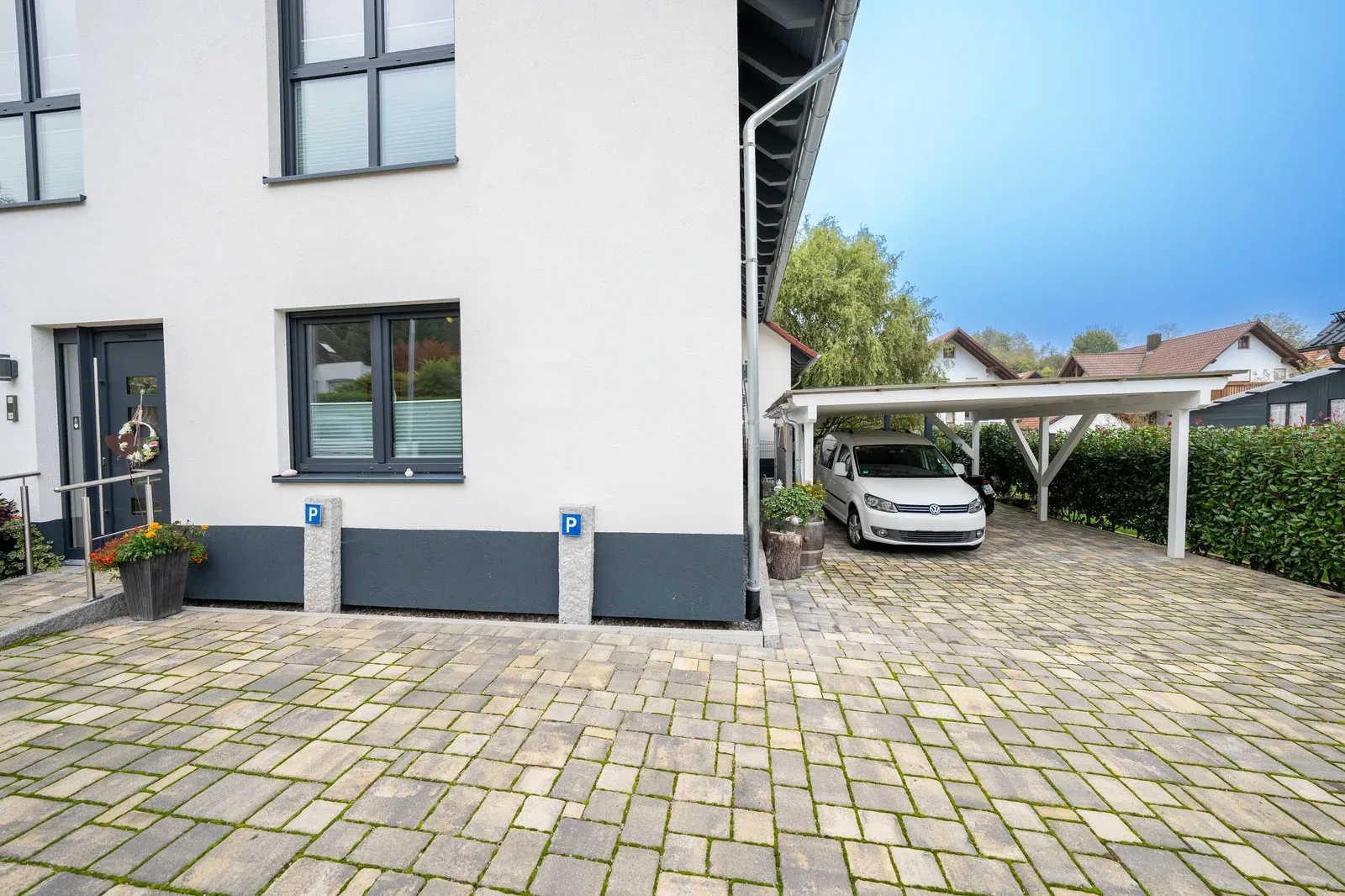 Gepflasterter Parkbereich am Haus mit Parkplatz-Schildern und Carport.