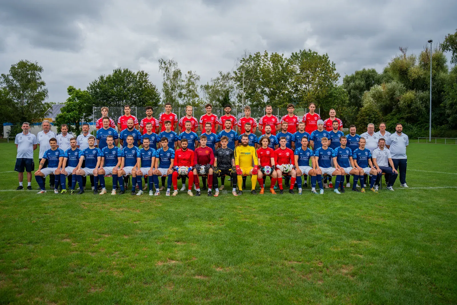 Mannschaftsfoto eines Fußballvereins: drei Reihen Spieler in blauen und roten Trikots auf dem Rasen.