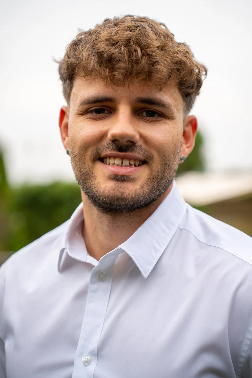 Freundliches Portrait eines jungen Mannes mit Locken und weißem Hemd im Freien.