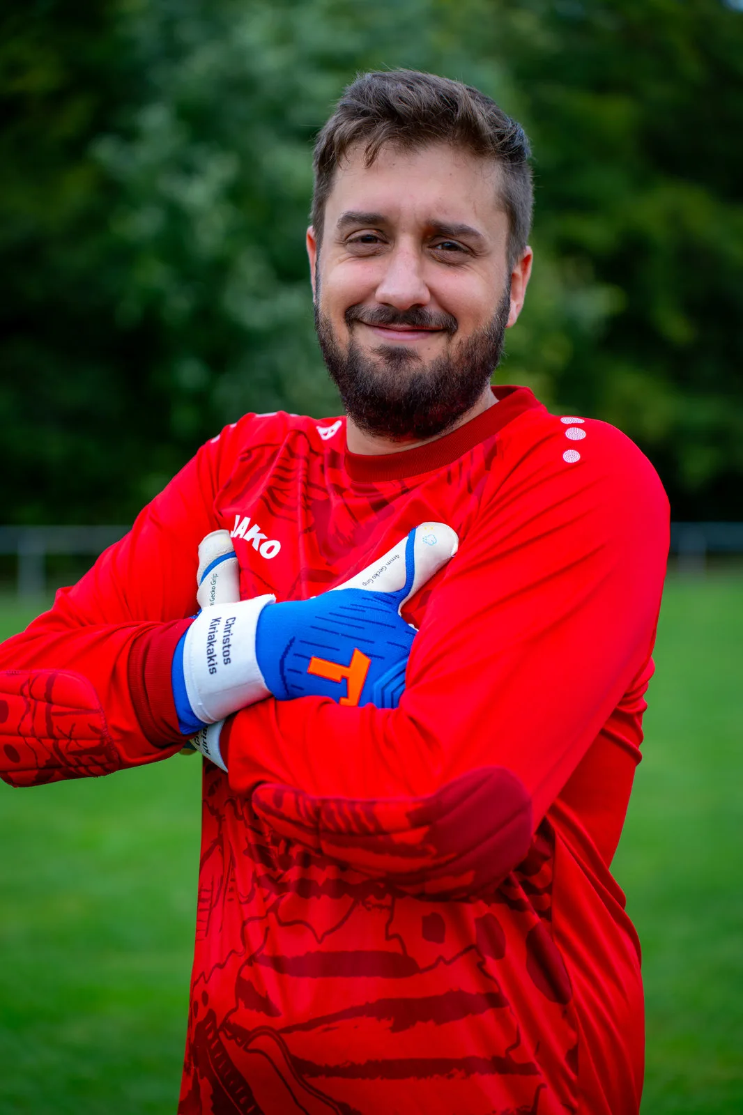 Portrait eines Torwarts im roten Trikot mit verschränkten Armen und Torwarthandschuhen.
