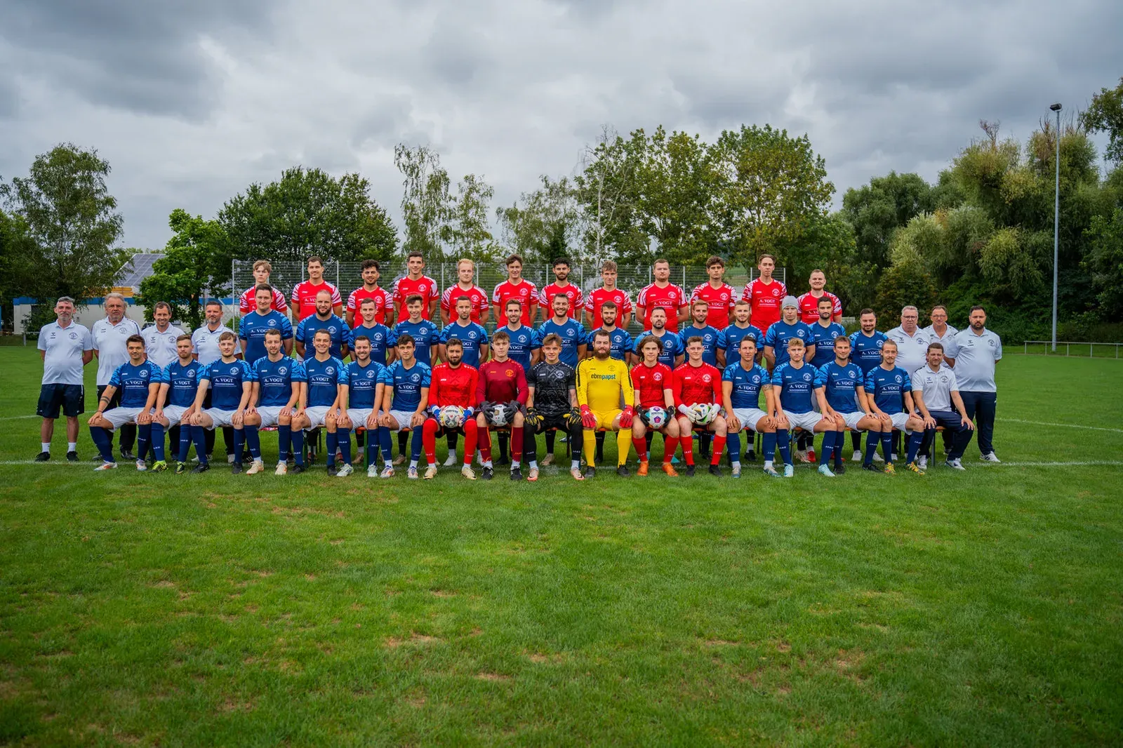 Gesamtaufnahme der Fußballmannschaft mit Trainern und Betreuern auf dem Rasen.