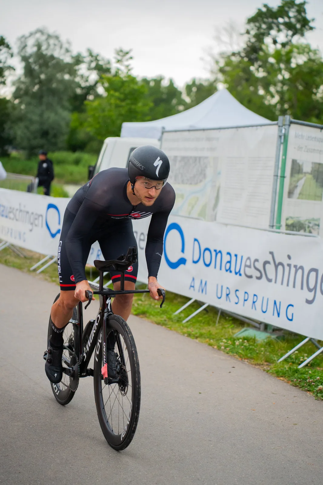 Ein Zeitfahrer beugt sich über den Aero-Lenker, hinter ihm die Banner des Radrennens.