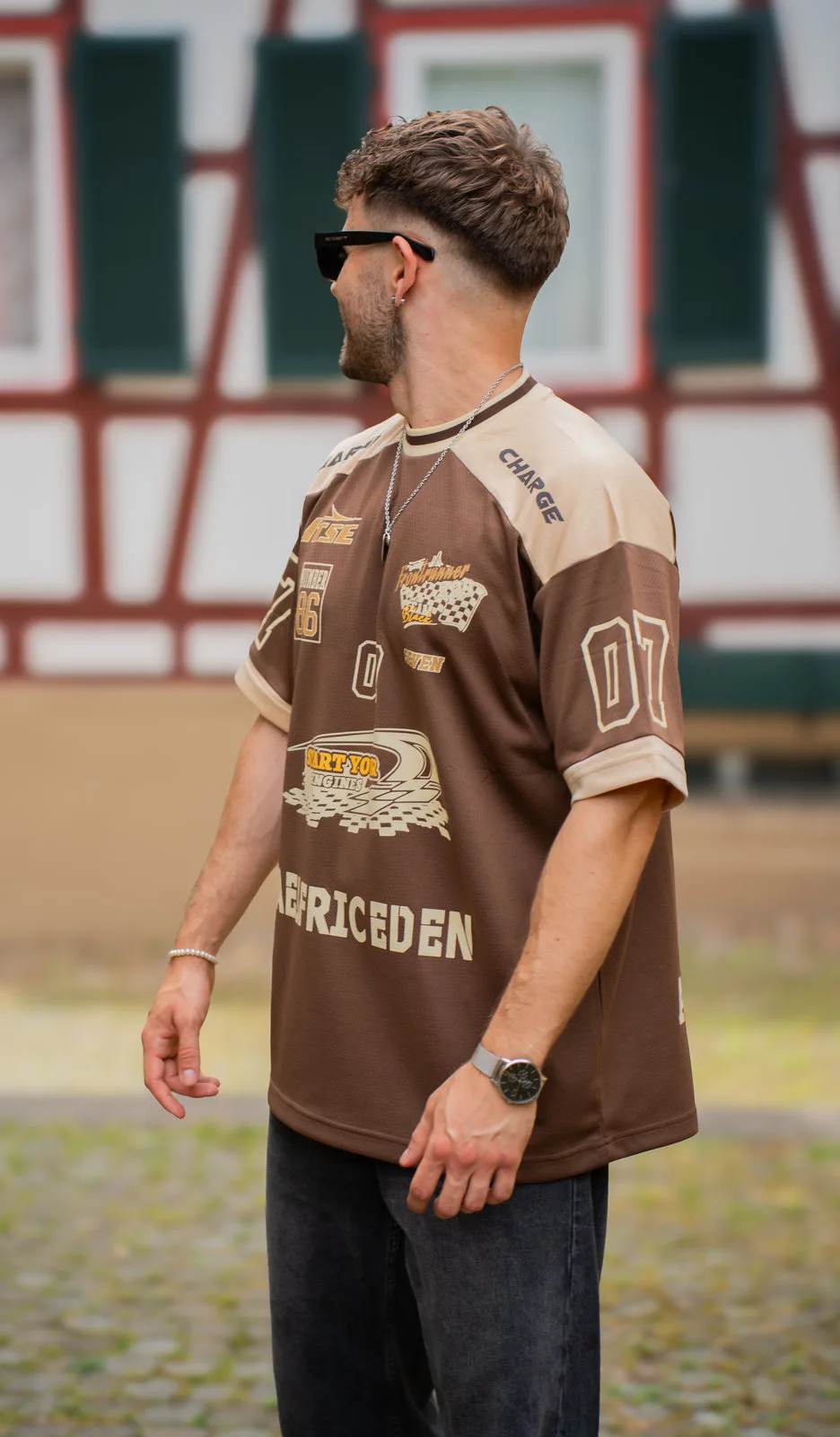 Ein junger Mann im braunen Football-Trikot steht seitlich vor einem Fachwerkhaus.