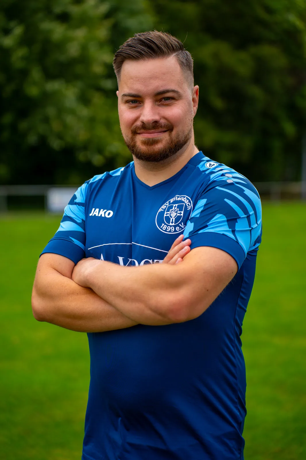 Portrait eines Fußballspielers im blauen Vereinstrikot mit verschränkten Armen.