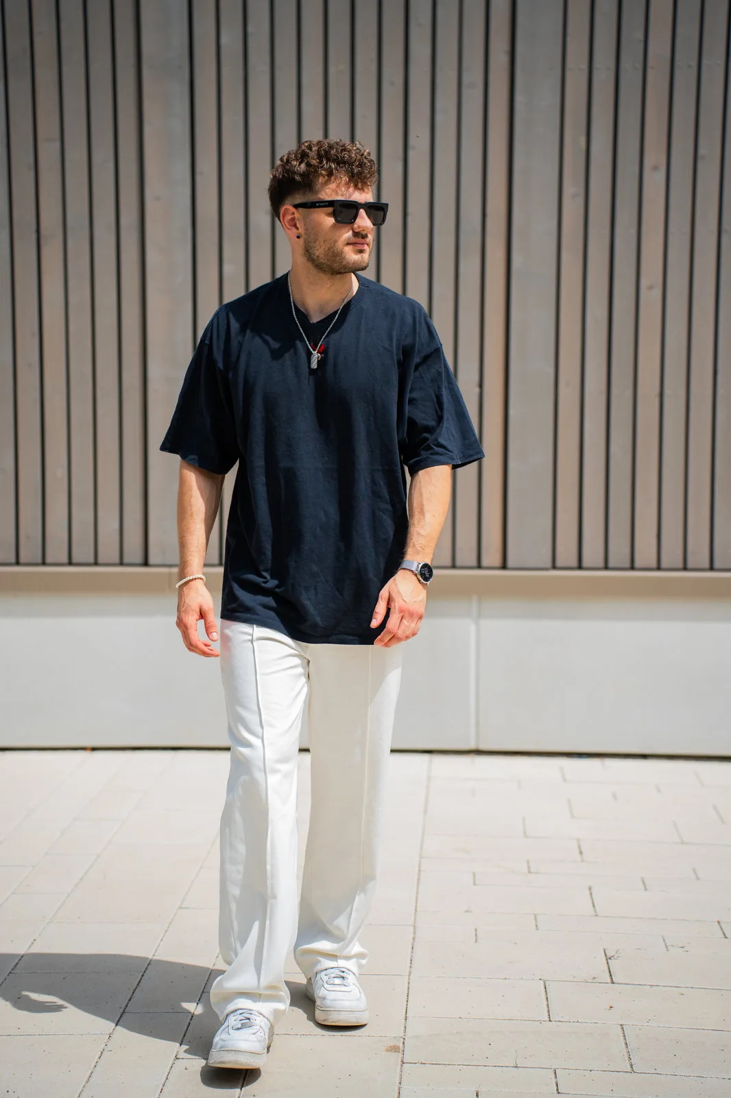 Ein junger Mann im dunklen Oversize-Shirt und weißer Hose geht über einen gepflasterten Platz.