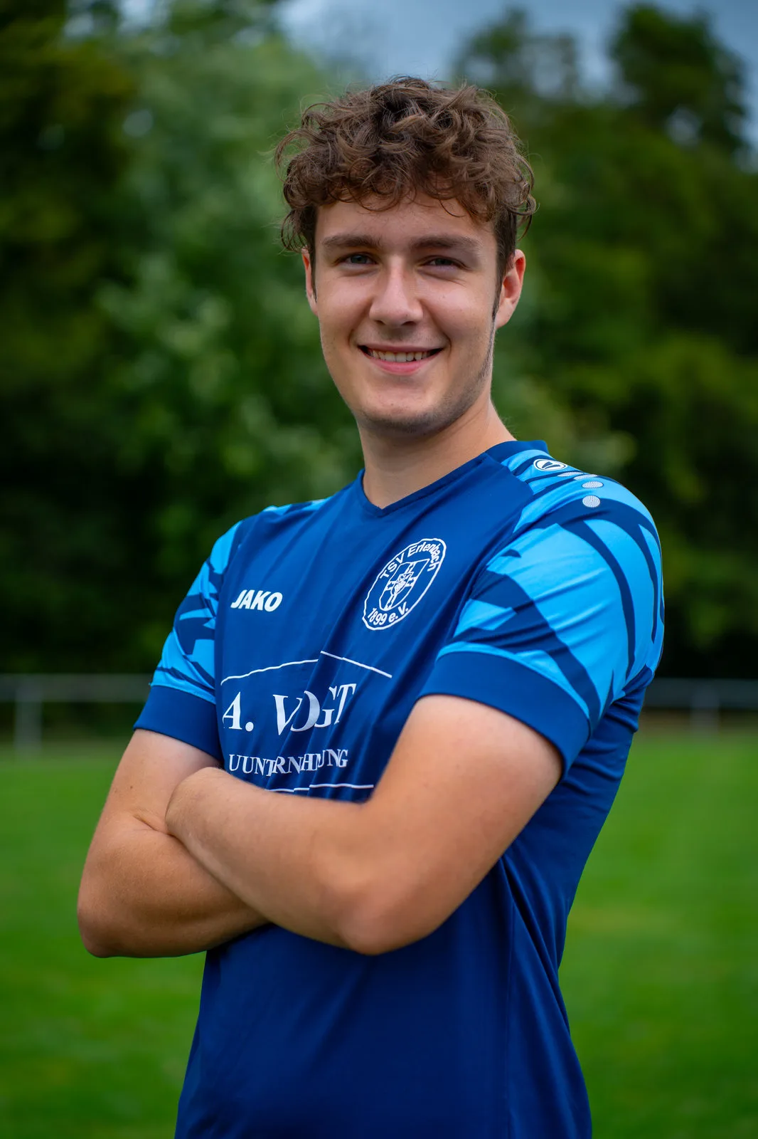 Lächelnder junger Fußballspieler mit Locken im blauen Vereinstrikot.